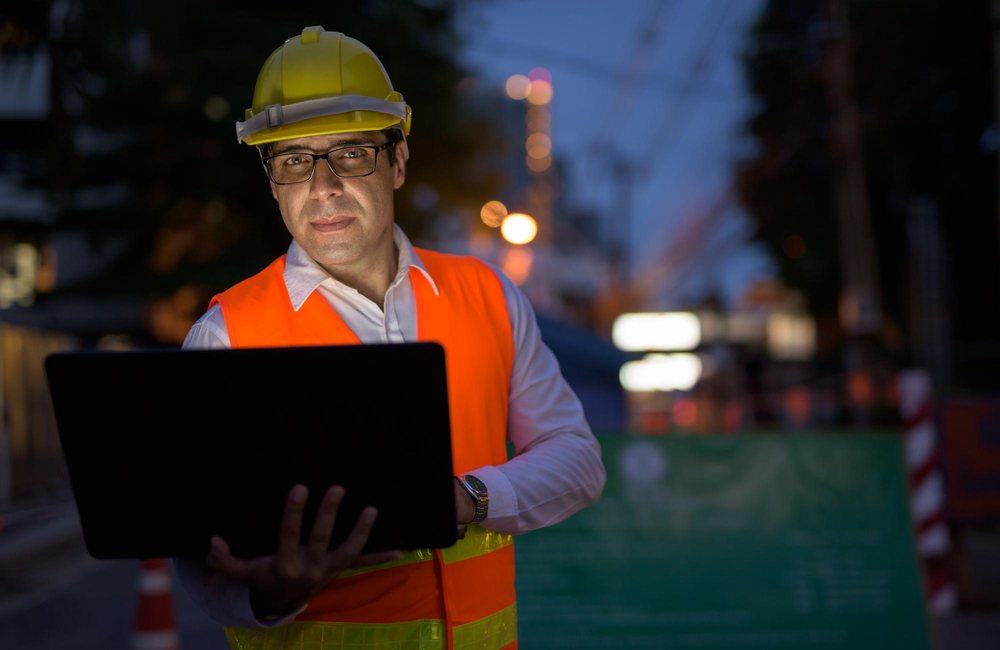 Profesional de SST con laptop en obra durante una sesión nocturna